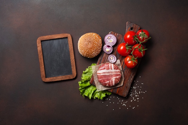 Hamburger ingredients raw cutlet, tomatos, lettuce, bun, cheese, cucumbers and onion on rusty background