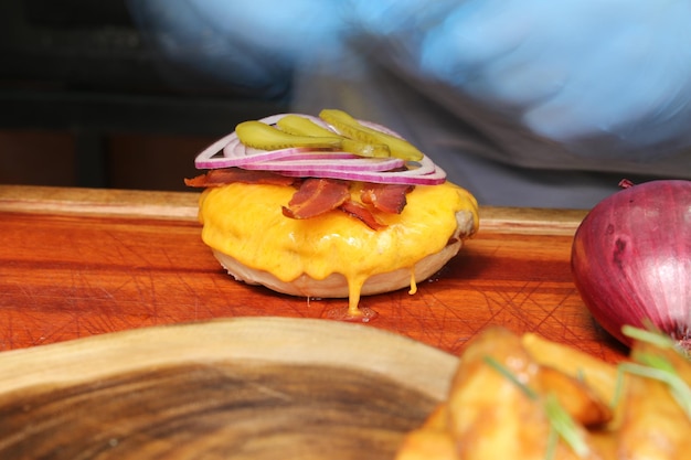 ハンバーガーはバーベキューグリルで作られましたチーズベーコンオニオンピクルスと木製の背景に