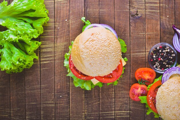 Hamburger met kaas vlees tomaten en uien en kruiden op houten achtergrond bovenaanzicht vrije ruimte