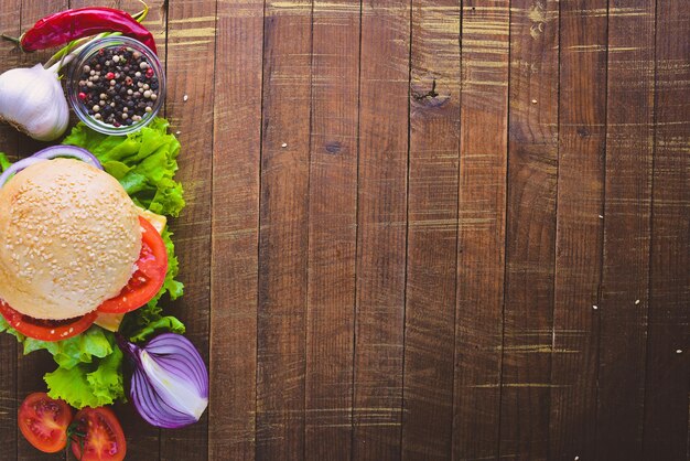 Hamburger met kaas vlees tomaten en uien en kruiden op houten achtergrond bovenaanzicht vrije ruimte