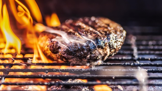 Foto hamburger su una griglia all'aperto con fiamme dal fuoco e vapore fumoso dalla carne