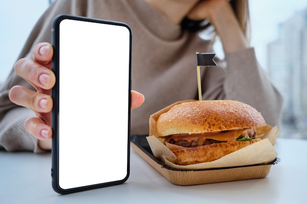 Hamburger on the table and a girl holding a smartphone with copy space.