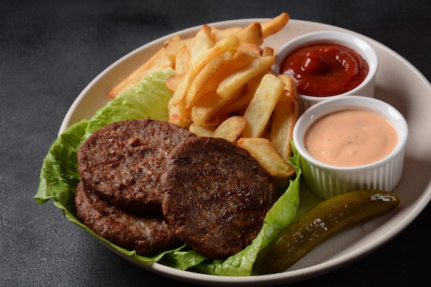 Hamburger vlees steaks frietjes en salade op zwarte achtergrond