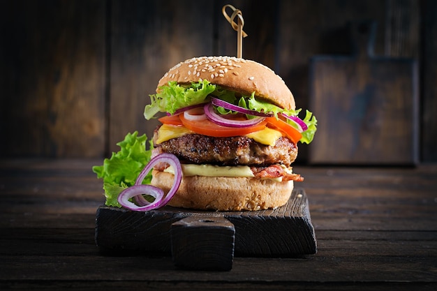 Hamburger with bacon, turkey burger meat, cheese, tomato and lettuce on wooden background. Tasty burger. Close up