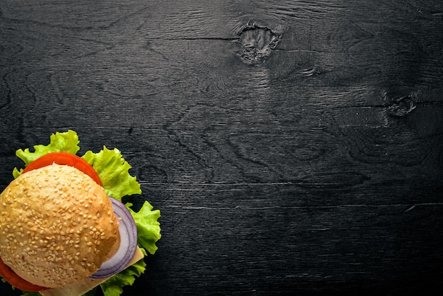 Hamburger con formaggio, carne, pomodori, cipolle ed erbe aromatiche su fondo in legno vista dall'alto spazio libero