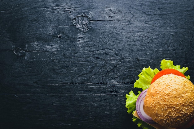 Гамбургер с сыром, мясом, помидорами, луком и зеленью на деревянном фоне Вид сверху Свободное пространство