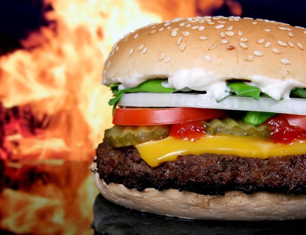 a hamburger with cheese and tomatoes on it is in front of a fire.