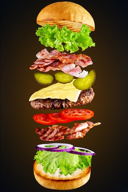 Foto hamburger con ingredienti volanti isolato su un buio. immagine ad alta risoluzione. ingredienti volanti per hamburger fatti in casa al buio. ottimo gustoso hamburger fatto in casa con ingredienti volanti