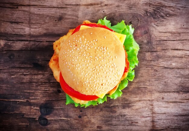 Hamburger con pomodoro fresco, insalata, formaggio e carne su un vecchio tavolo di legno.