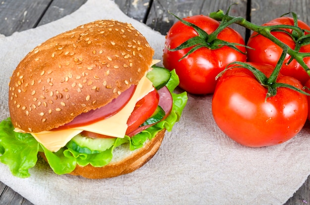 Hamburger con prosciutto formaggio cetriolo pomodori e insalata su un tovagliolo di lino accanto a un ramo di rosso pomodoro succoso