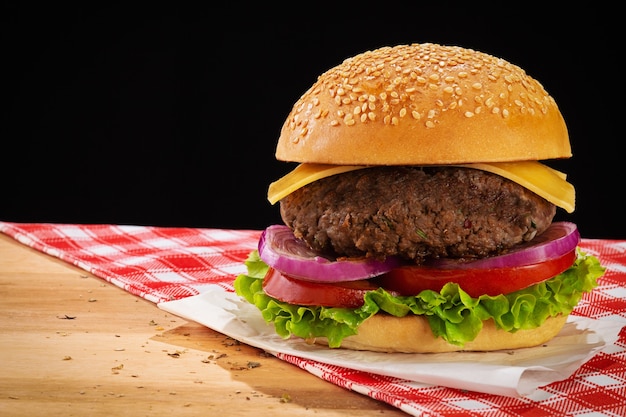 Hamburger con lattuga, pomodoro, cipolla rossa e formaggio. base in legno con tessuto a quadretti rossi. sfondo nero e spazio per il testo.