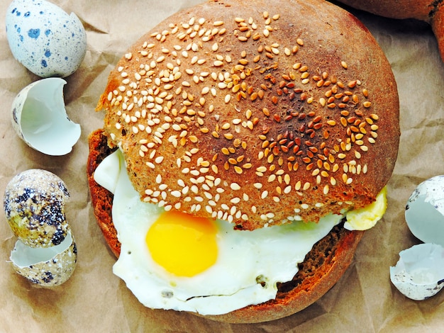 Hamburger with quail eggs. Rye bun with sesame. Close up. Fresh hot bun with fried quail eggs.