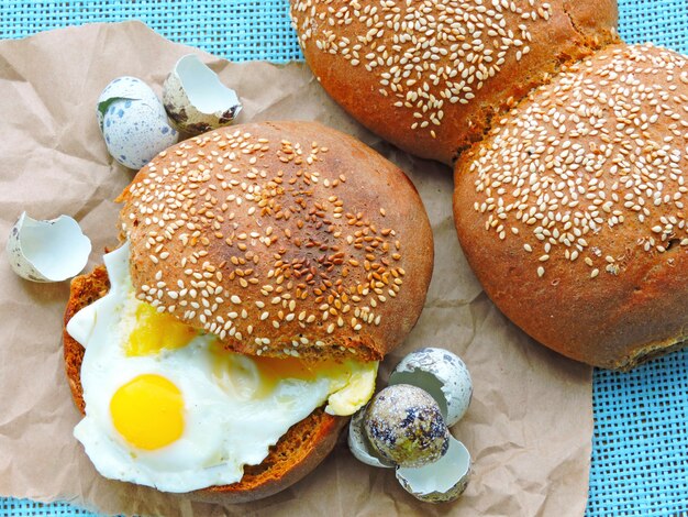 Hamburger with quail eggs. Rye bun with sesame. Close up. Fresh hot bun with fried quail eggs.