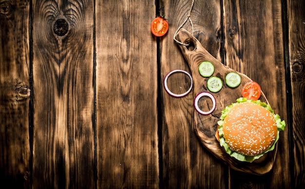 Hamburger with tomatoes, onions and meat on the Board. On wooden background.   Top view.