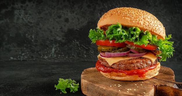 Hamburger with vegetables, ketchup, cheddar and pickled cucumber on wooden board