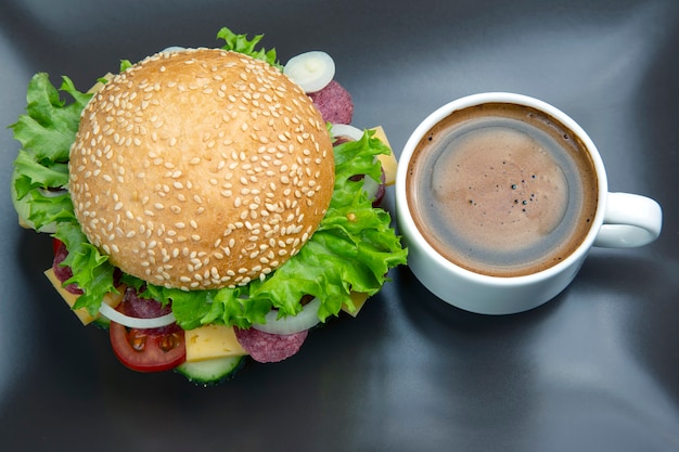 Hamburger with vegetables and sausage and coffee on a gray