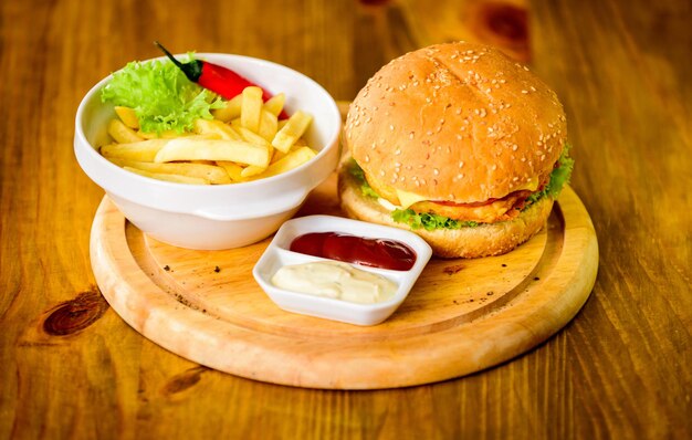 Hamburgermenu. Hoogcalorisch tussendoortje. Hamburger en frietjes en tomatensaus op een houten bord. Fastfood-concept. Hamburger met kaasvlees en salade. Dieet ondermijnende maaltijd. Heerlijke burger met sesamzaadjes.