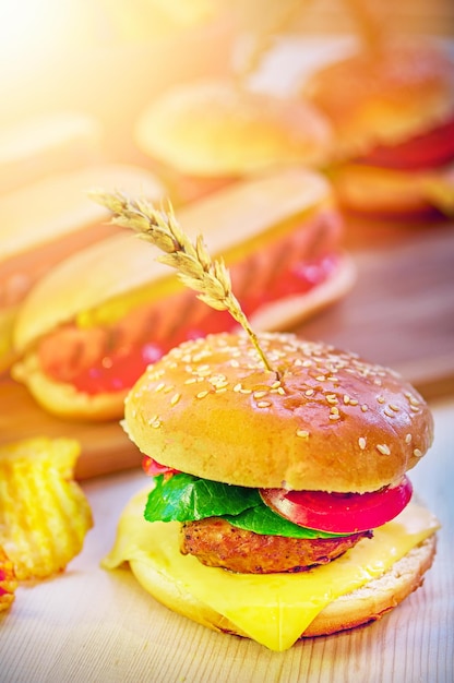 Hamburgers chips and hot dog on wooden board in sunny cafe