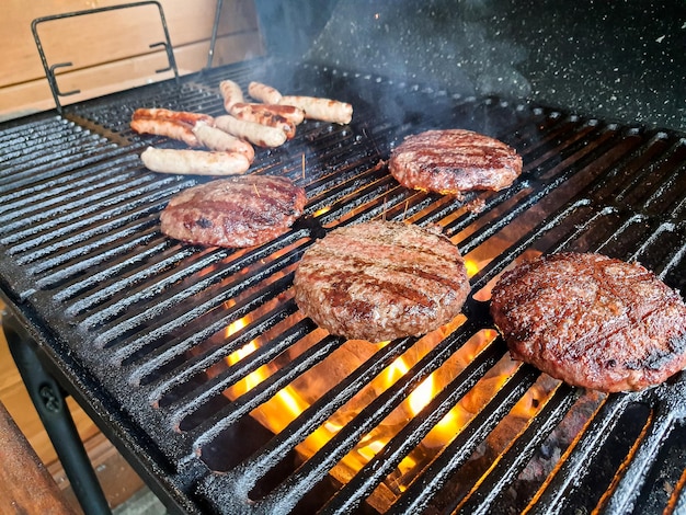 Hamburgers grillen op houtskoolgrill Sappige hamburgers van rundvlees die sissen boven hete vlammen op de barbecue