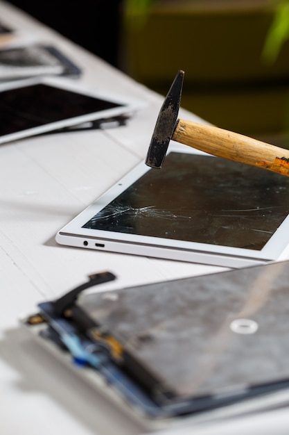 The hammer hits the broken touchscreen tablet, suggesting that it is about to replace it. Broken glass tablet repair