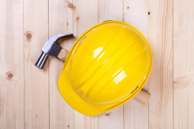 Hammer and yellow hardhat on wood background