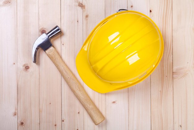 Hammer and yellow hardhat on wood background