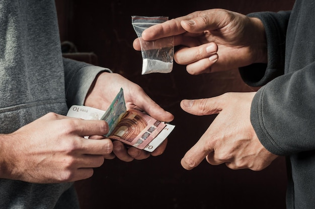 Hand of addict man with money buying dose of cocaine or heroine or another narcotic from drug dealer Drug abuse and traffic concept