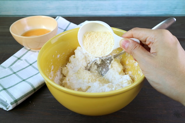 Hand adding Parmesan cheese onto dough in mixing bowl for baking Brazilian cheese bread