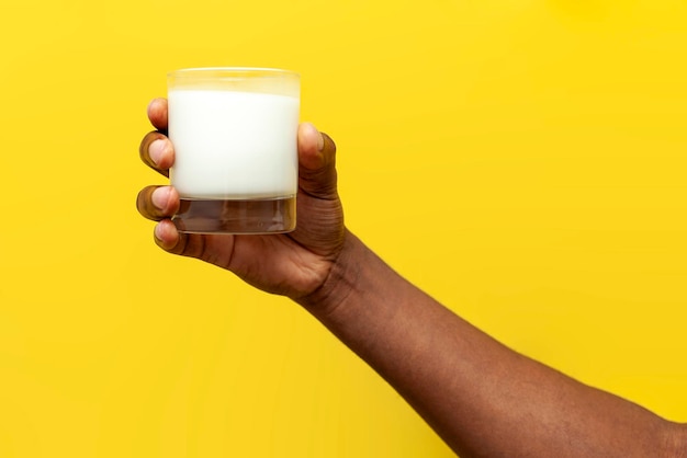 Hand of african american man holds glass of milk on yellow isolated background