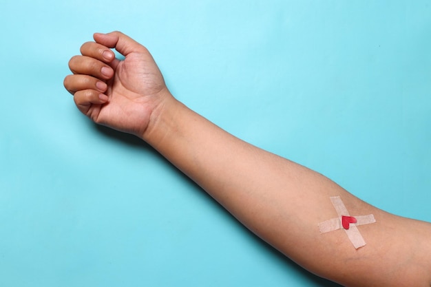 Рука после сдачи крови с гипсовым сердцем на синем фоне Концепция переливания крови