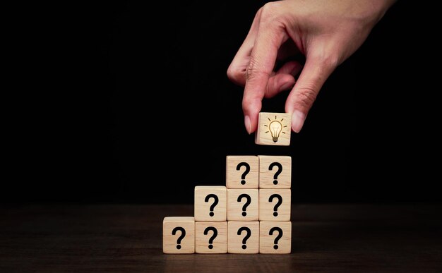 Hand arranged wooden blocks stacked into stairs with icon question mark and lampthinking with quest