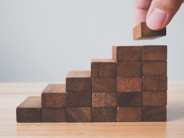 Hand arranging wood block stacking as step stair. Ladder career path for business