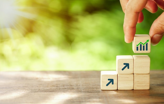 Hand arranging wood block stacking as step stair with arrow up on the natural background Business