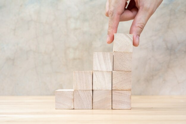 Hand arranging wood block stacking as step stair on wooden table. Business concept for growth success process. Copy space