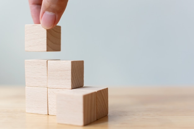 Hand arranging wood block stacking as step stair on wooden table. Business concept for growth success process.