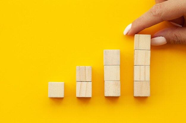 Hand arranging wood cube stacking as up stairs on yellow background