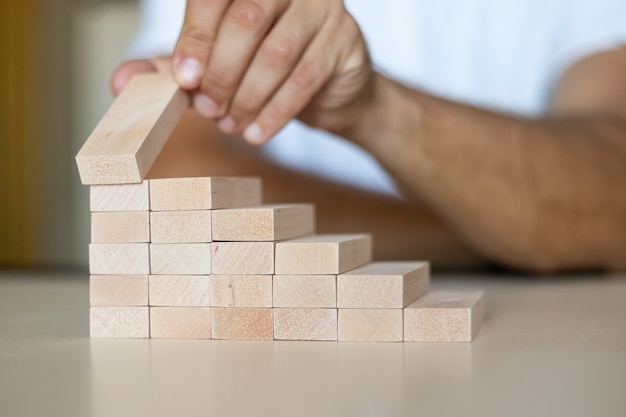 Hand arranging a wooden stacking block like a stepped ladder on a wooden table. Business concept for a successful growth process. Copy space