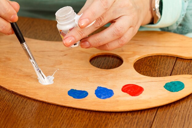 Hand of the artist laying white paint over palette using a paintbrush