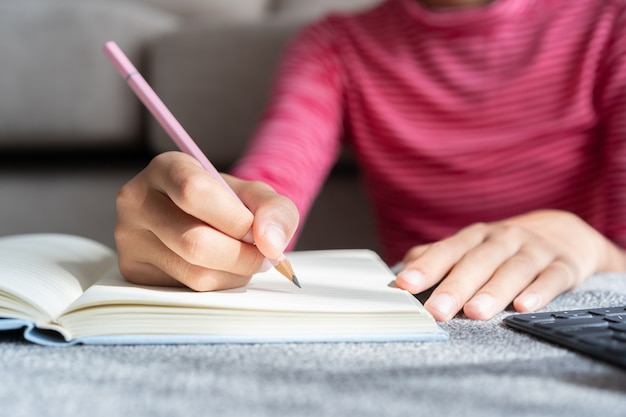 Foto la mano della ragazza asiatica sta studiando in linea via internet scrive il taccuino e fa i compiti mentre era seduto nel soggiorno