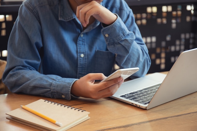 Mano della donna asiatica che utilizza smartphone sulla tavola di legno nella caffetteria