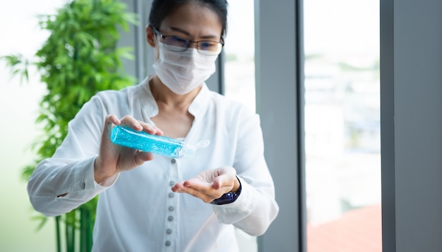 Hand of Asian woman wearing surgical mask squeeze alcohol gel rub hand while work at home