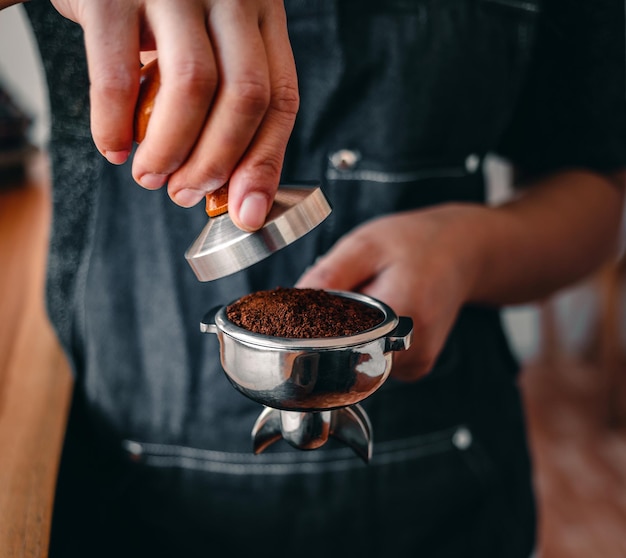 Photo hand barista or coffee maker holding portafilter and coffee tamper making an espresso coffee