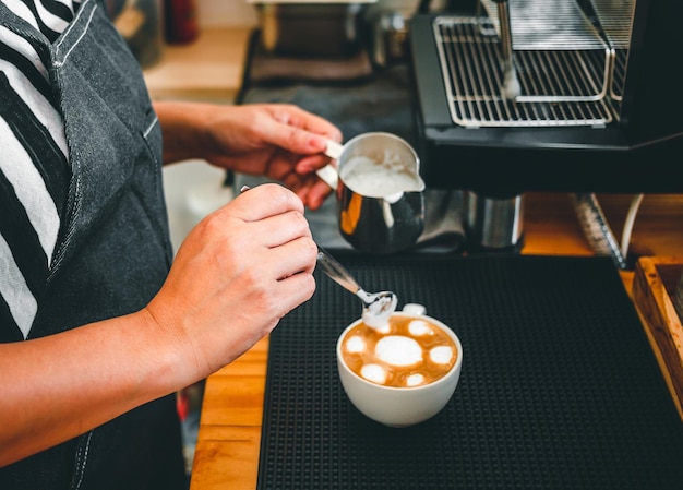 コーヒーカプチーノメニューのジャグでミルクを蒸す準備をしている喫茶店のバリスタの手