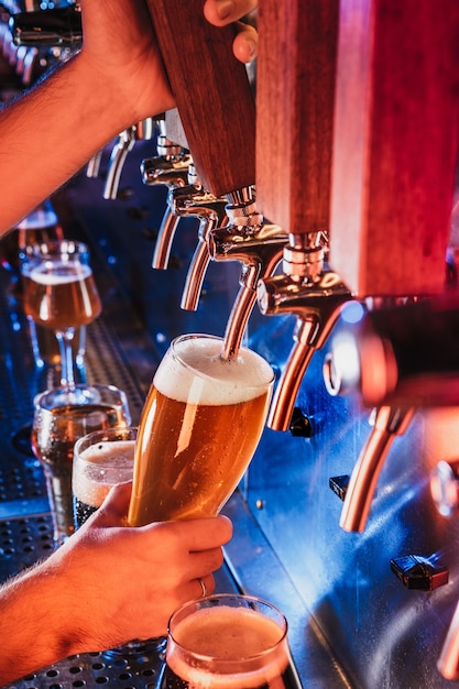 Photo hand of bartender pouring a large lager beer in tap. bright and modern neon light, males hands. pouring beer for client. side view of young bartender pouring beer while standing at the bar counter.