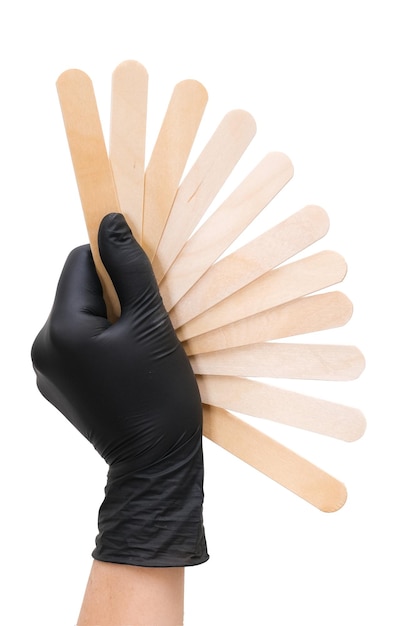 Hand in a black glove holds wooden sticks for depilation on white isolated background fan