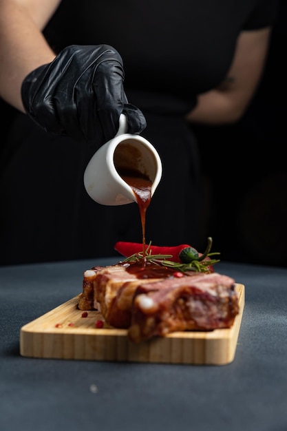 A hand in a black glove pours sauce over a piece of meat