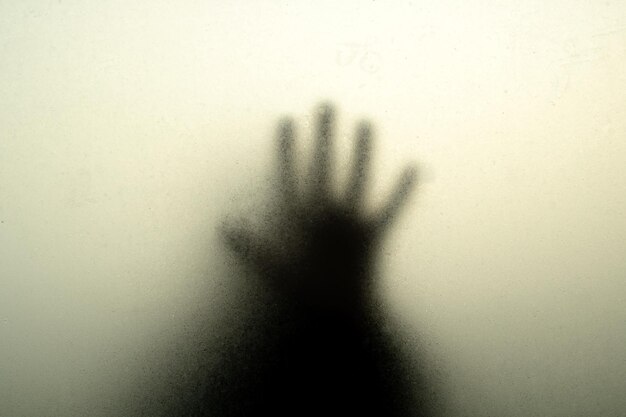 Hand black silhouette behind misted glass in the shadows