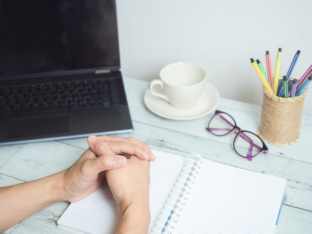 Hand on blank paper notebook with laptop and coffee and glasses
on the desk workspace concept