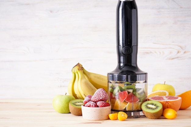 Hand blender and accessories with sliced fruit on a wooden background, place for text. Close up.