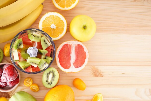 Hand blender and accessories with sliced fruit on a wooden background, place for text. Flat lay.